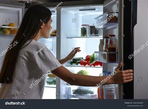 stock-photo-young-woman-looking-into-modern-refrigerator-at-night-2441300303.jpg